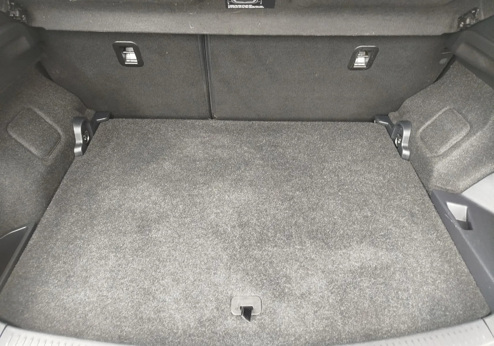 Vue intérieure du coffre spacieux et tapissé de moquette grise de la Toyota Auris HSD 136h SkyBlue 2015.