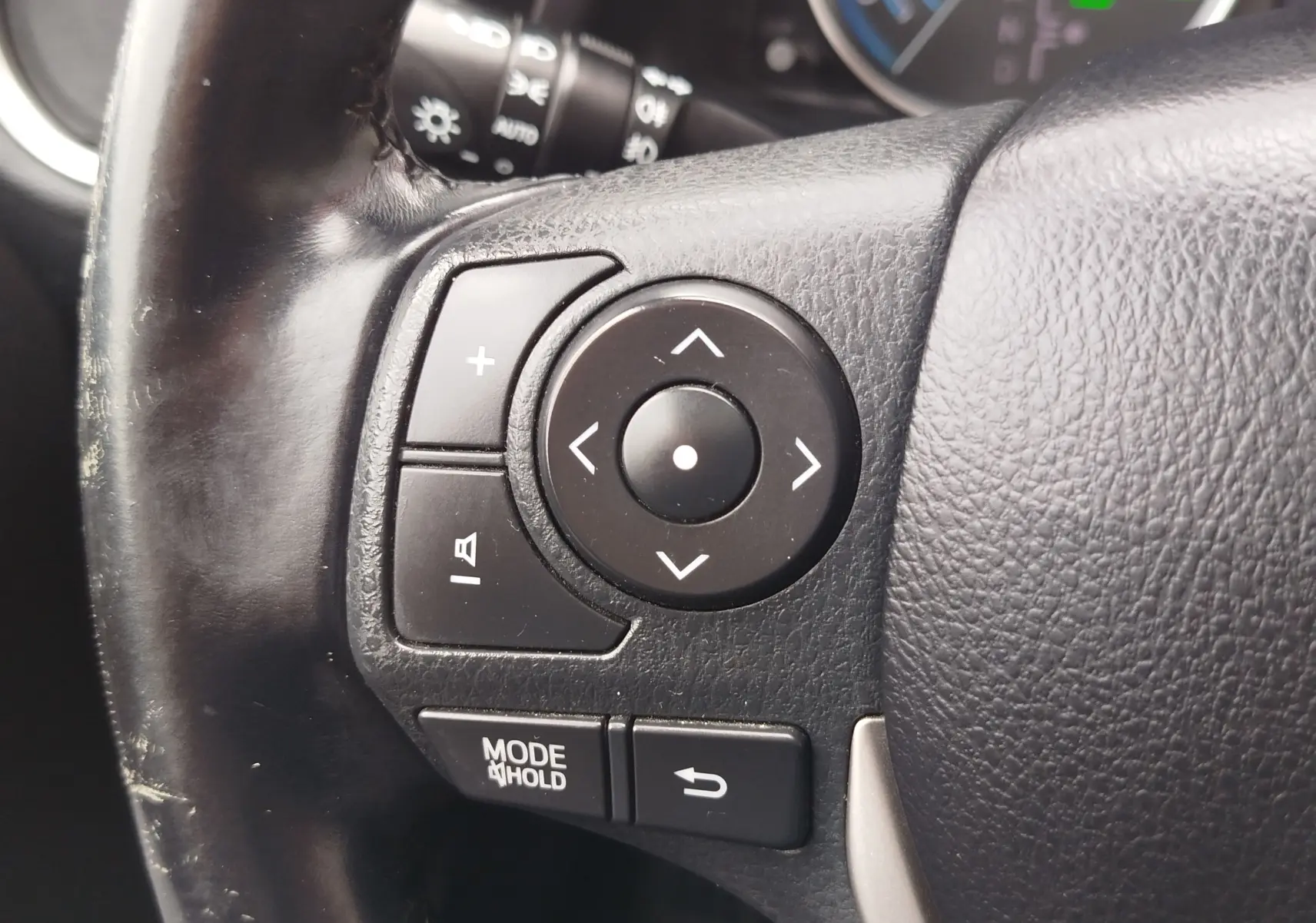 Gros plan sur les commandes multifonctions noires du volant en cuir noir d'une Toyota Auris gris aluminium, version hybride 2015.