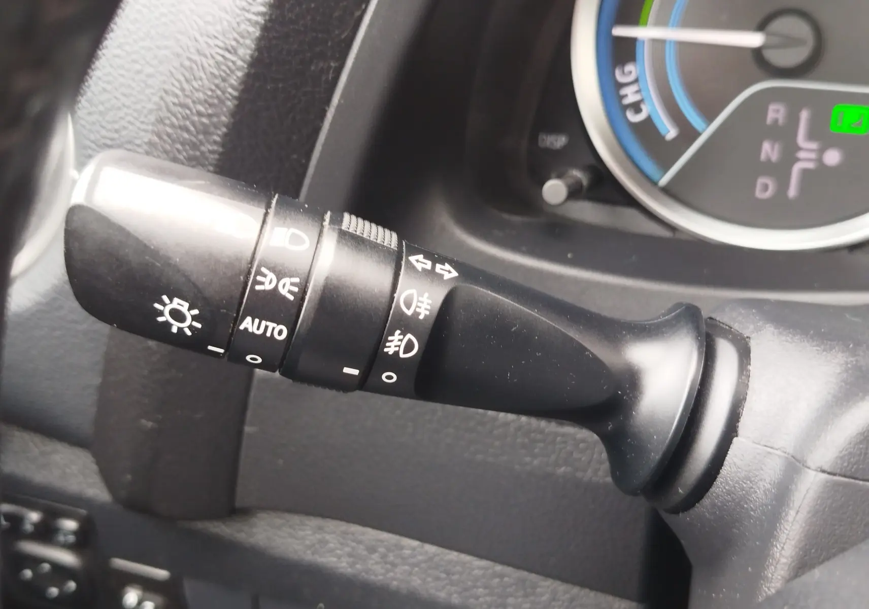 Gros plan sur la manette des feux et clignotants noire dans l’habitacle d’une Toyota Auris gris aluminium, tableau de bord partiellement visible.