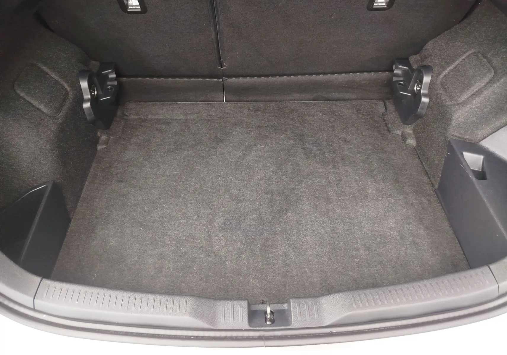 Vue intérieure du coffre vide de la Toyota Auris HSD 136h gris aluminium, montrant la moquette et les fixations arrière.
