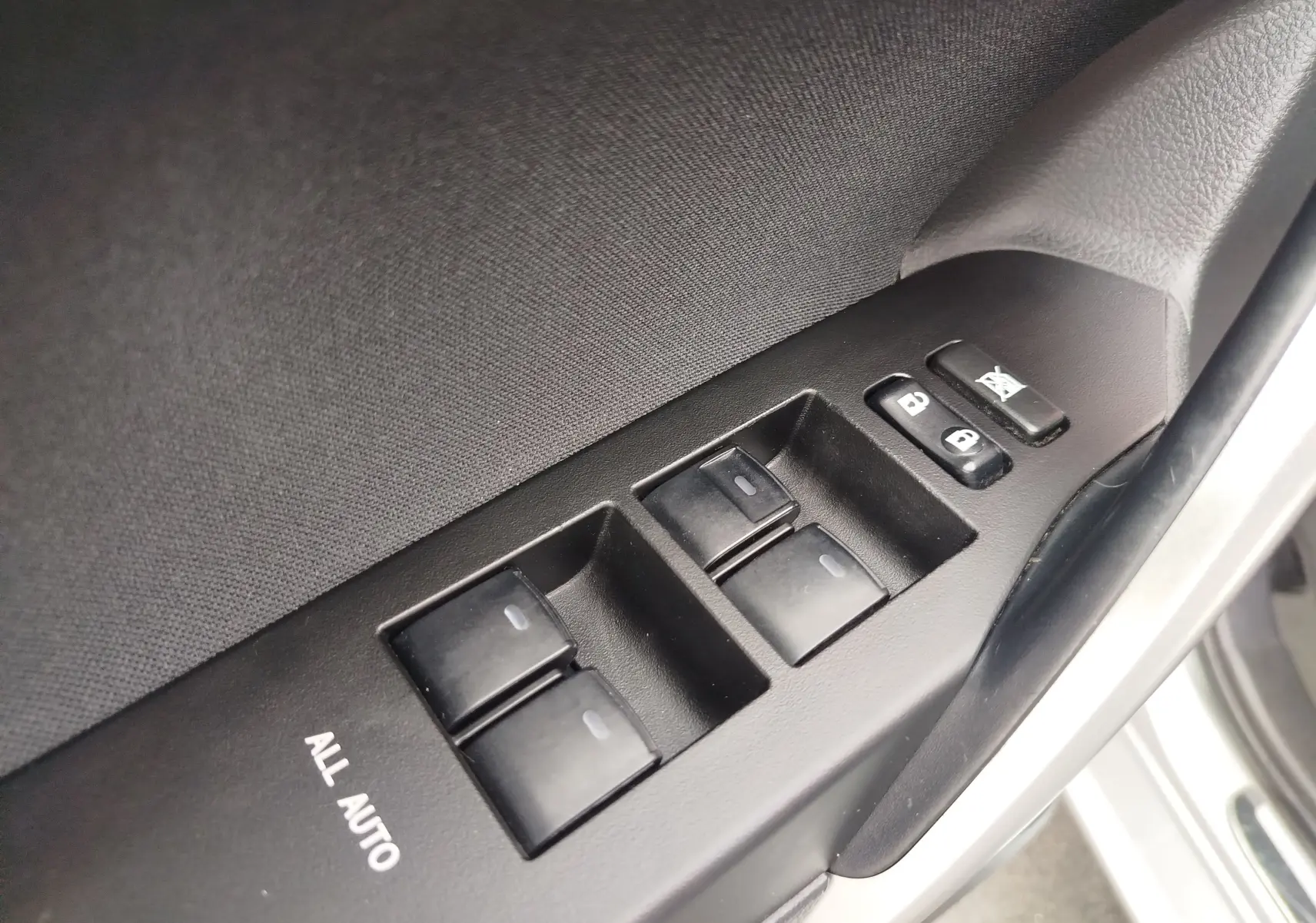 Gros plan sur les commandes de lève-vitres et verrouillage sur la porte côté conducteur d'une Toyota Auris gris aluminium.