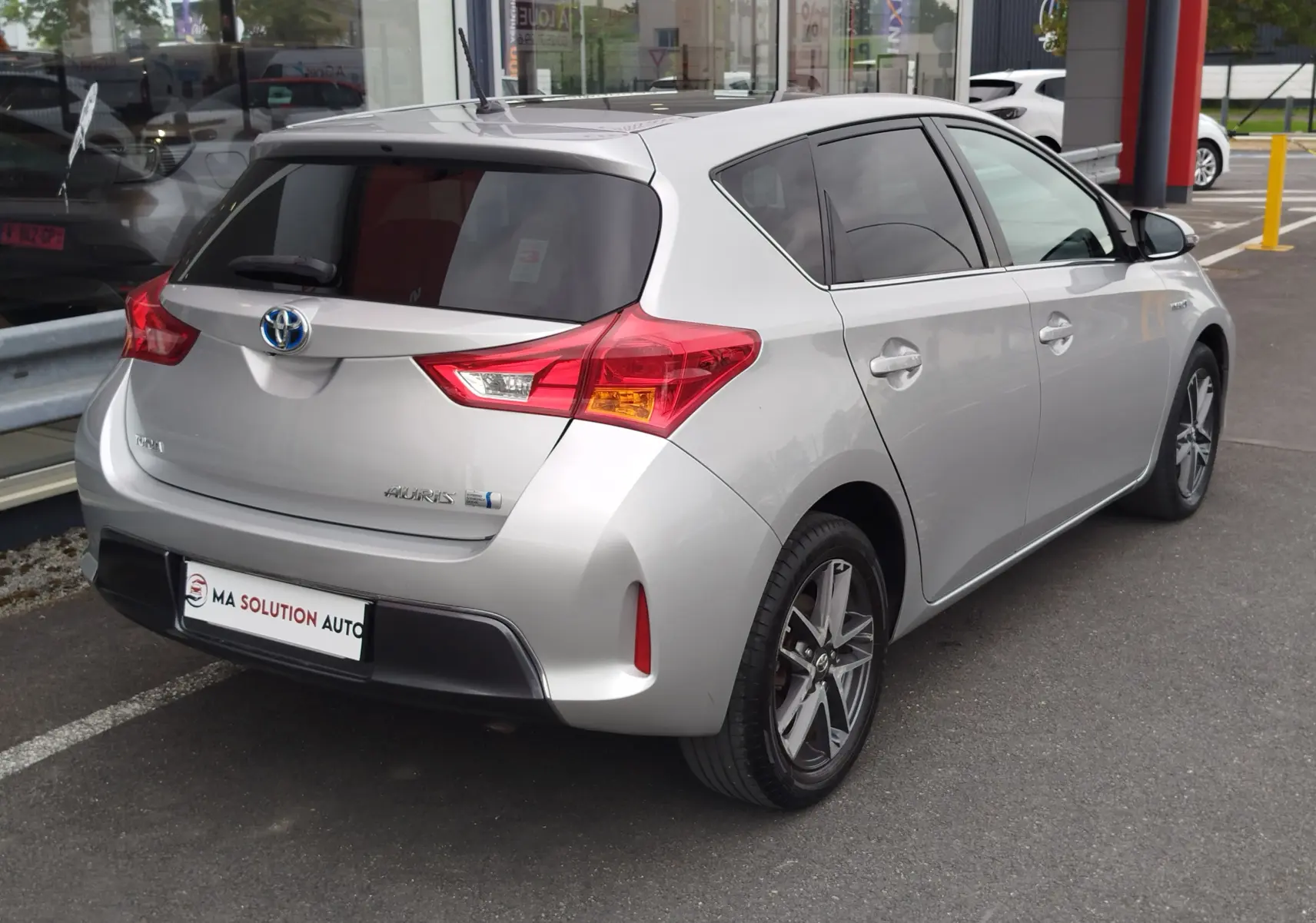 Toyota Auris gris aluminium vue 3/4 arrière droit, avec vitres teintées et feux arrière distinctifs rouges.