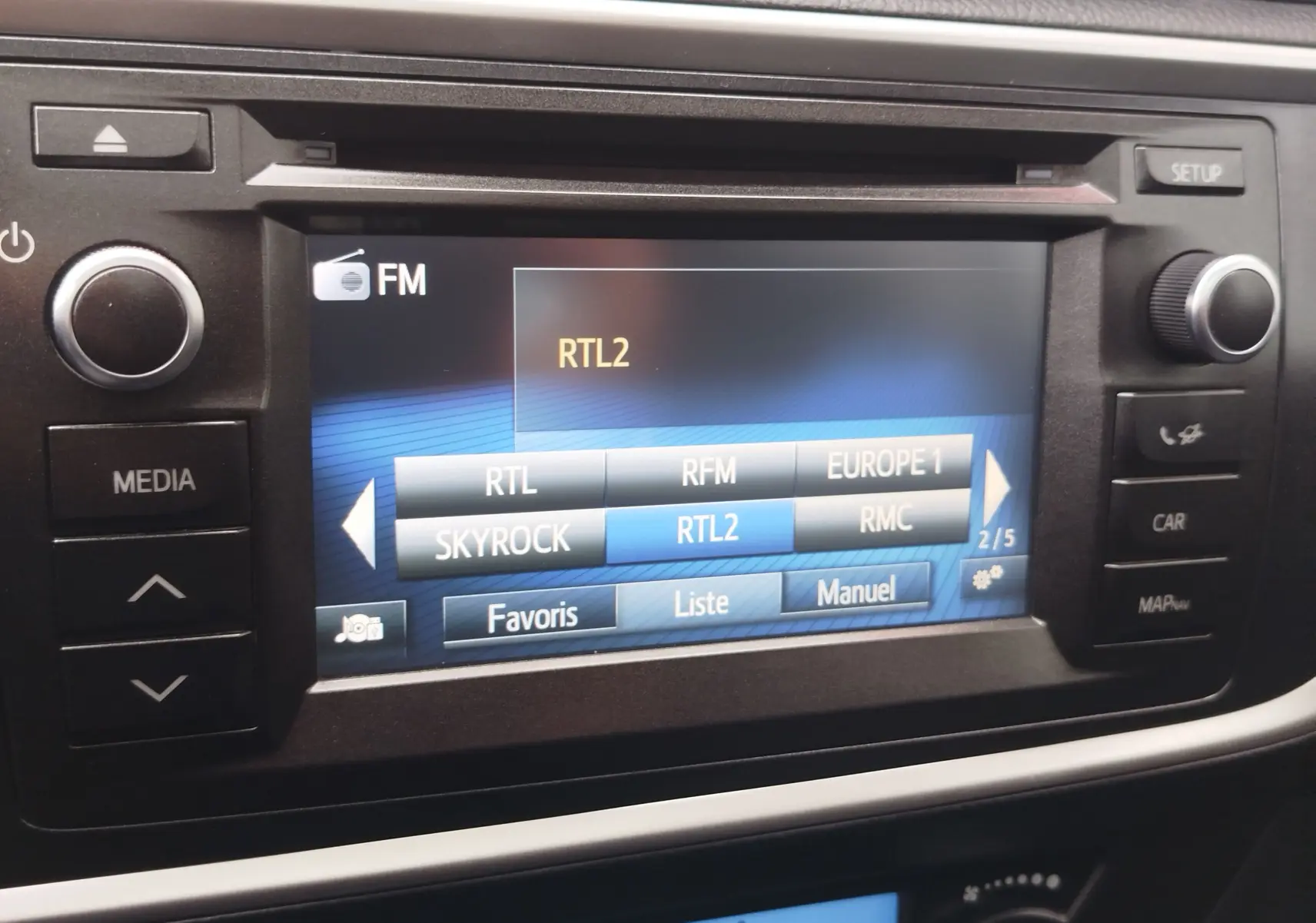 Gros plan sur l’écran multimédia de la Toyota Auris HSD 136h 2015, affichant les stations radio FM avec boutons autour.