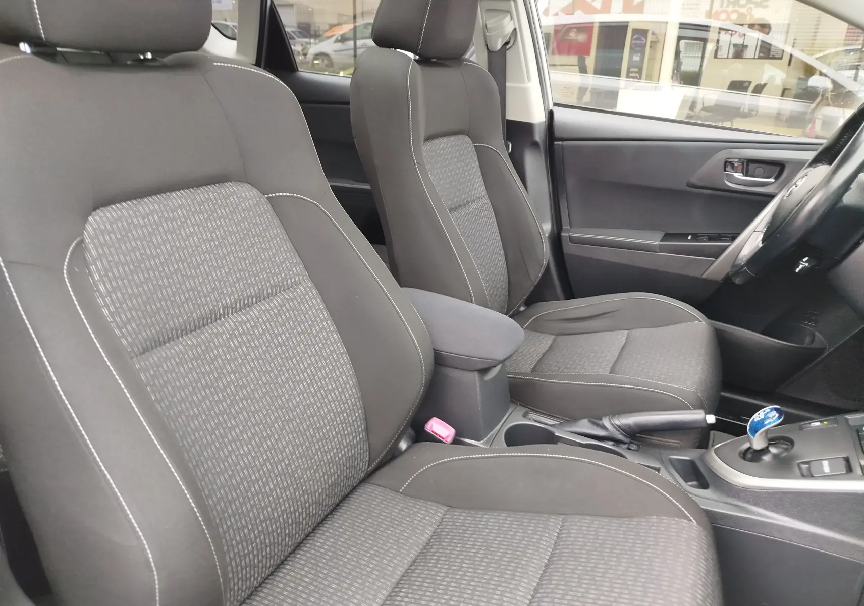 Vue intérieure côté conducteur de la Toyota Auris HSD 136h 2015, sièges tissu gris foncé avec coutures blanches.