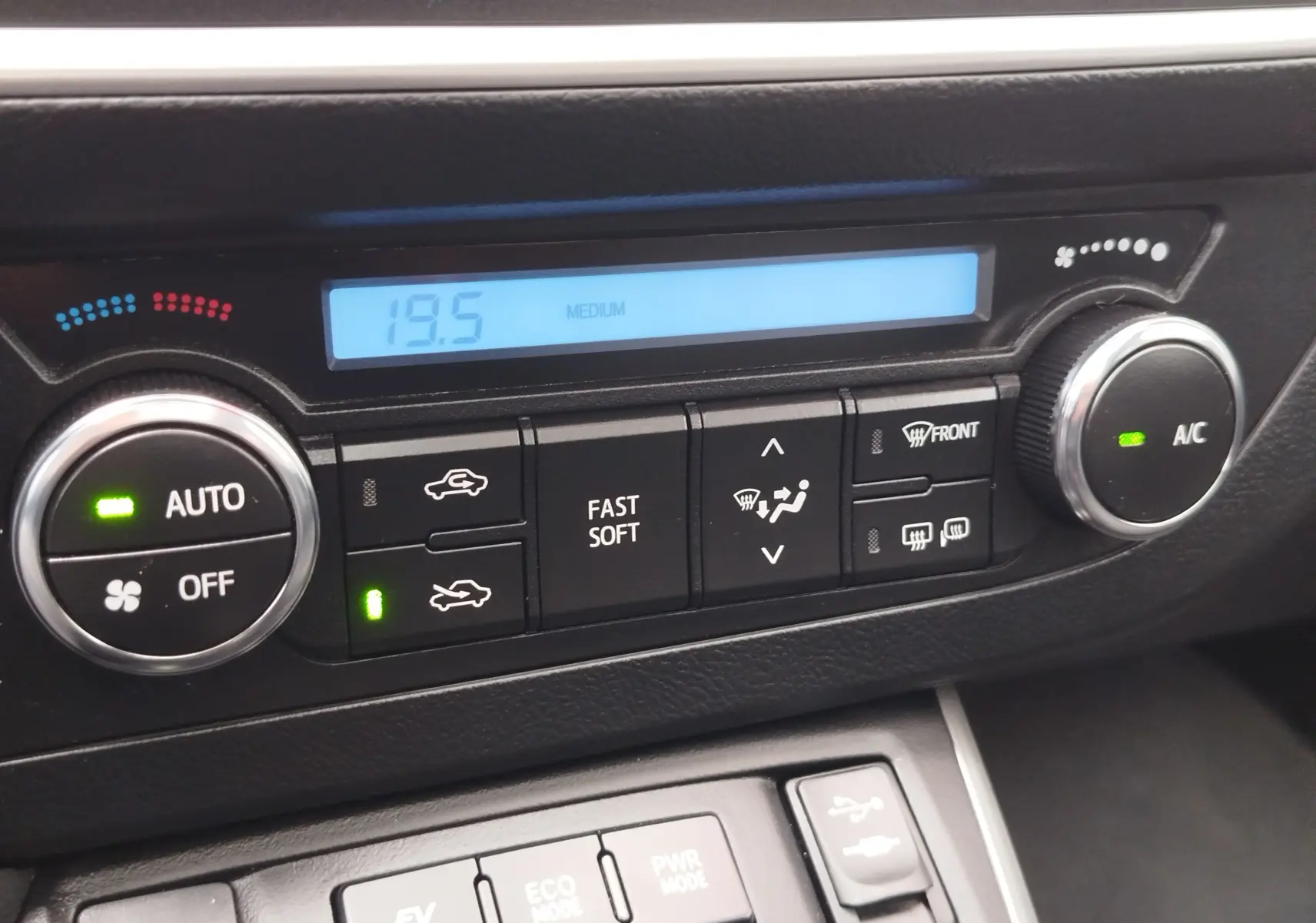 Détail de la console centrale de la Toyota Auris HSD 136h gris aluminium, montrant les commandes de climatisation et modes de conduite.