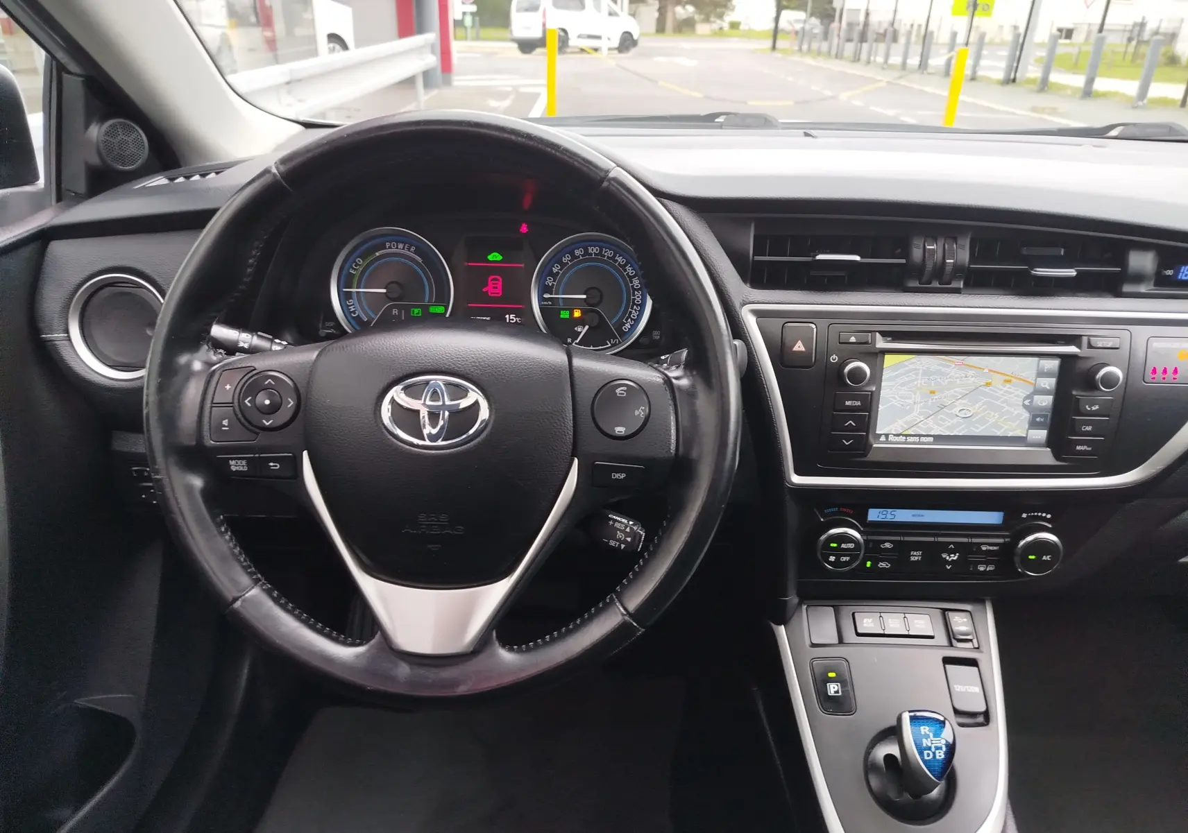 Vue intérieure du tableau de bord et volant noir de la Toyota Auris HSD 136h avec écran de navigation allumé.