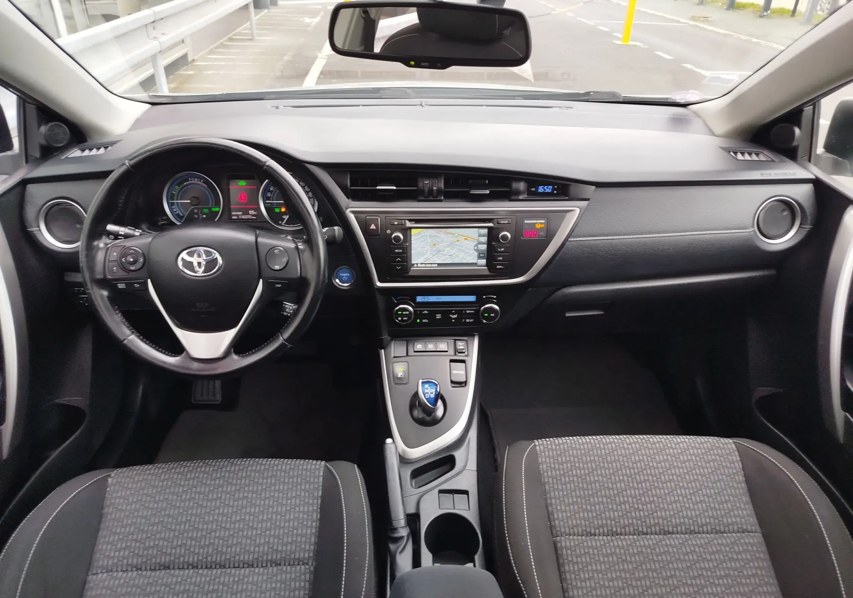 Vue intérieure frontale du tableau de bord et volant noir de la Toyota Auris hybride 2015 avec écran GPS et commandes au volant.
