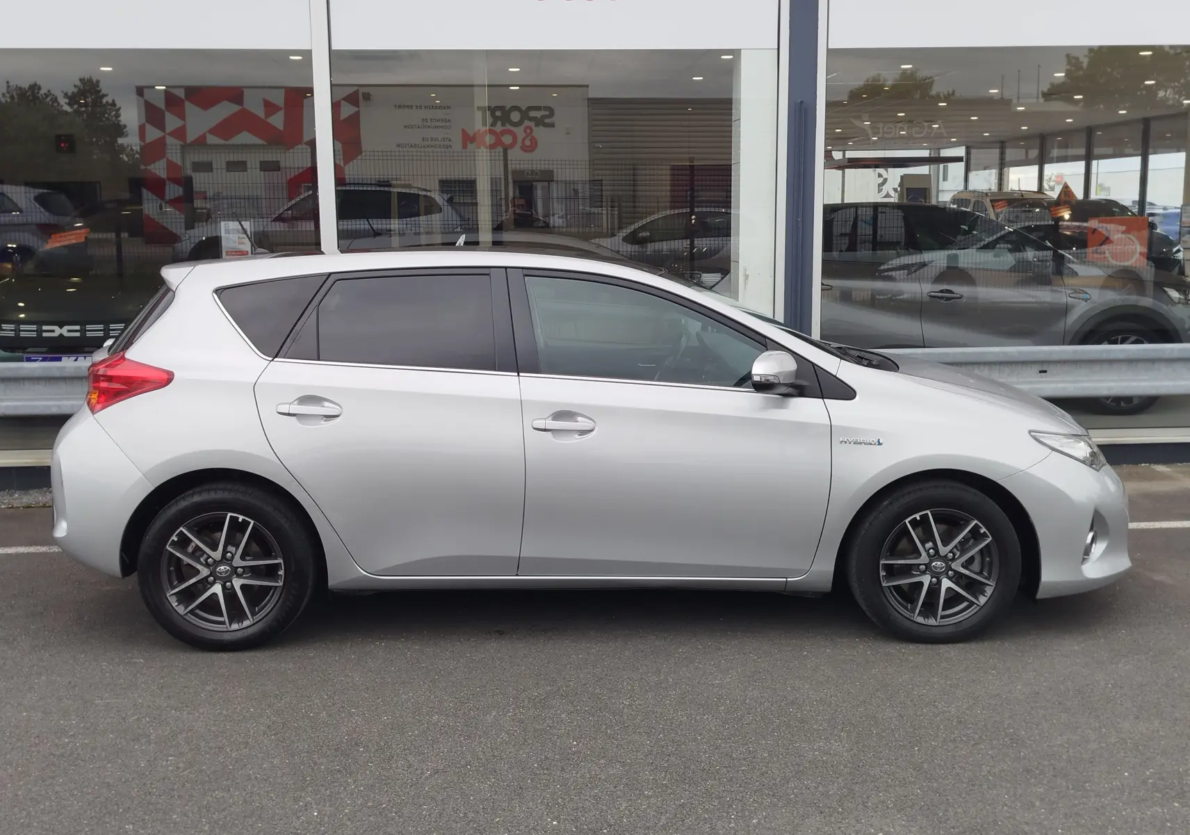 Profil droit d'une Toyota Auris gris aluminium de 2015, version hybride avec jantes alliage et vitres teintées.