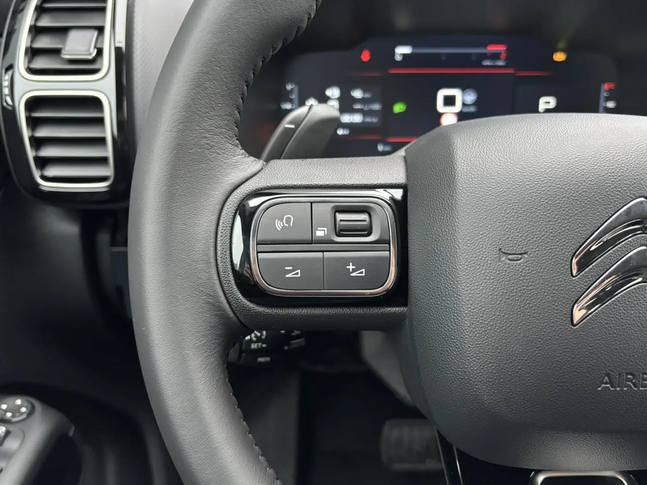 Gros plan sur le volant en cuir noir du Citroën C5 Aircross 2025 avec commandes intégrées et tableau de bord numérique flou.