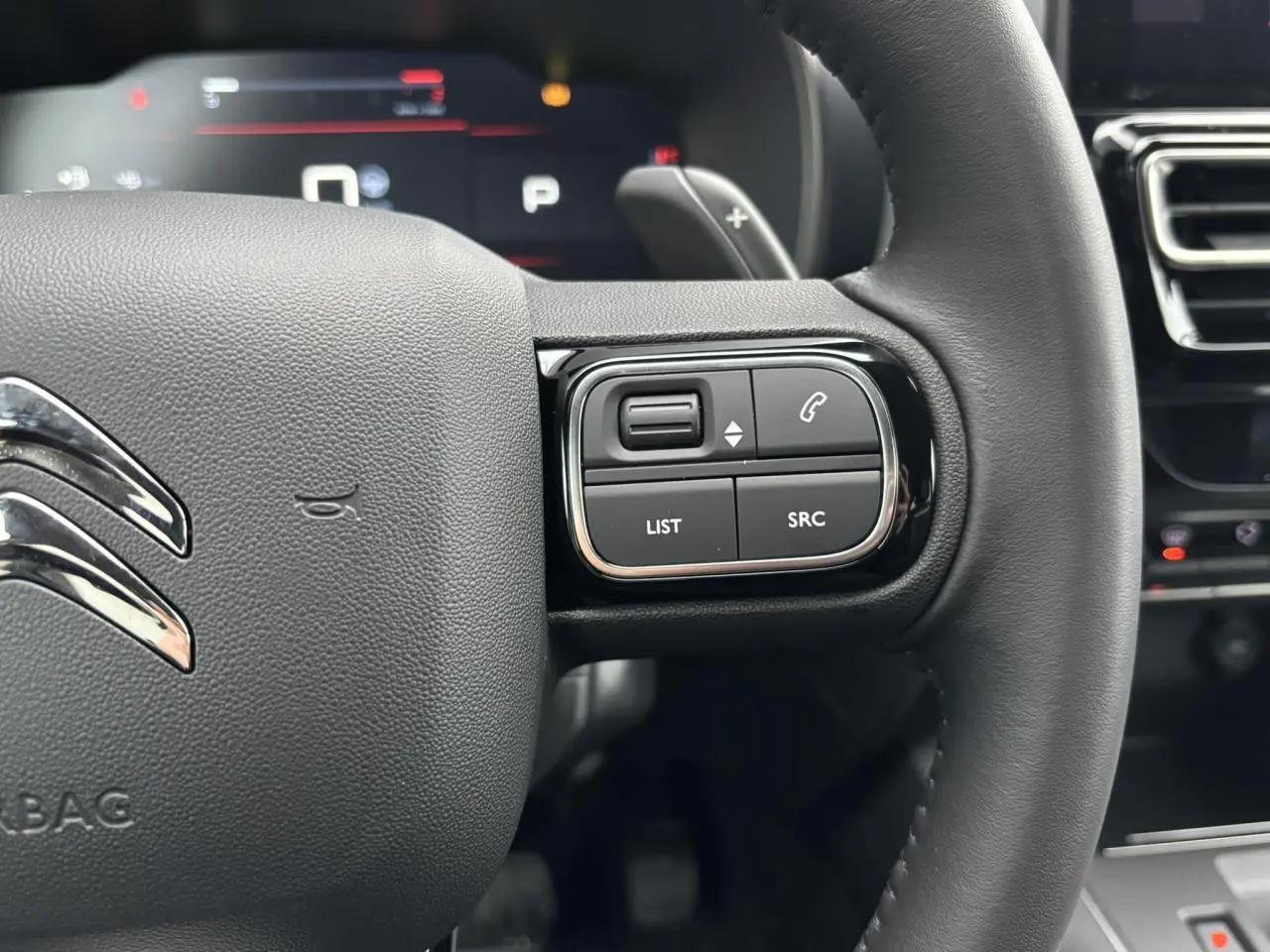 Gros plan sur le volant noir du Citroën C5 Aircross 2025, avec commandes intégrées côté droit et logo chromé central.