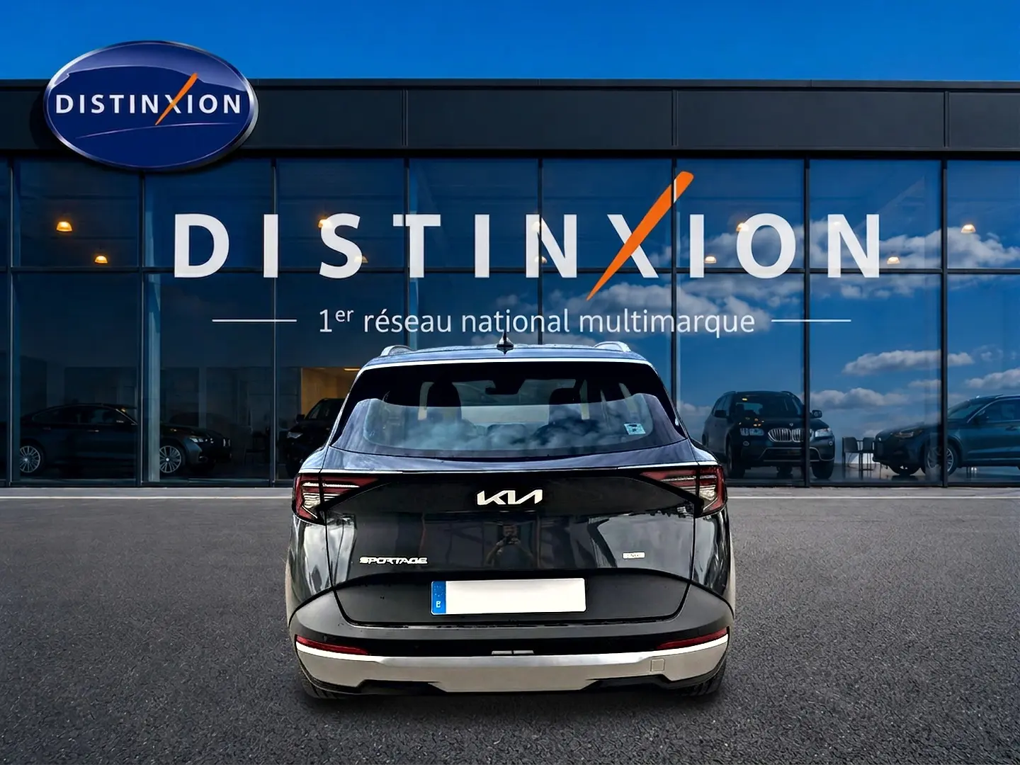 Vue arrière d'un Kia Sportage gris eclipse 2026 garé devant une vitrine avec logo Distinxion.
