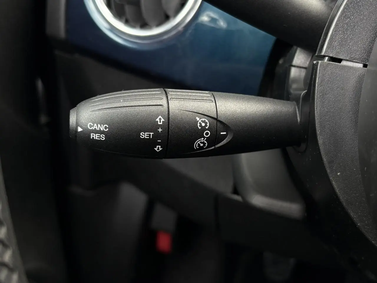 Gros plan sur la commande de régulateur de vitesse à gauche du volant dans l’habitacle bleu du Fiat 500 Hybrid 2024.