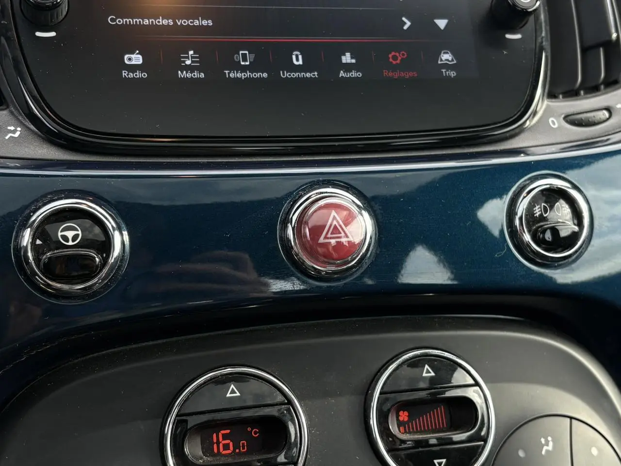 Gros plan sur la console centrale bleu Dipinto de la Fiat 500 Hybrid 2024 avec commandes clim et bouton de warning rouge.