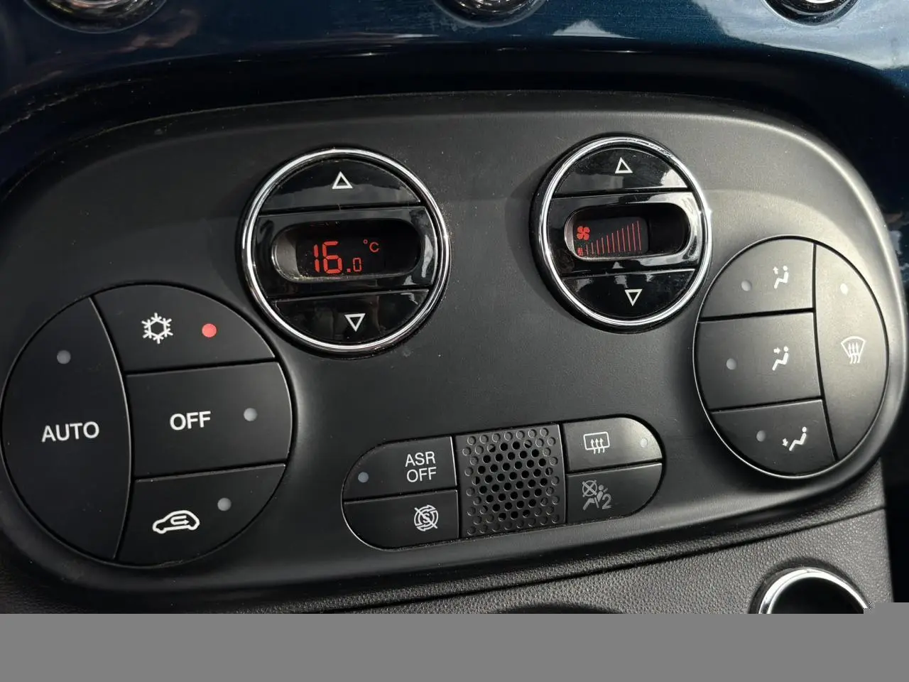 Gros plan sur la commande de climatisation digitale de la Fiat 500 Hybrid 70, affichant 16°C, avec boutons noirs et détails rouges.