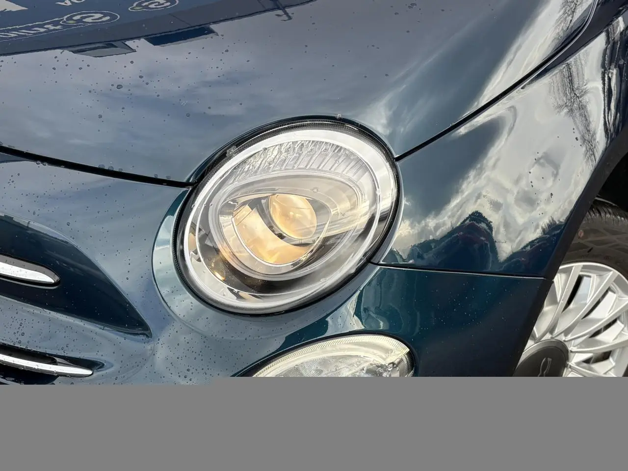 Gros plan sur le phare avant gauche d'une FIAT 500 Hybrid 70 bleu Dipinto avec jante alliage 15 pouces visible.