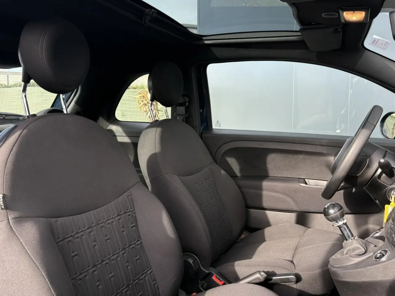 Vue intérieure côté droit de la Fiat 500 Hybrid 70 2024 avec sièges tissu noir et toit panoramique ouvert.