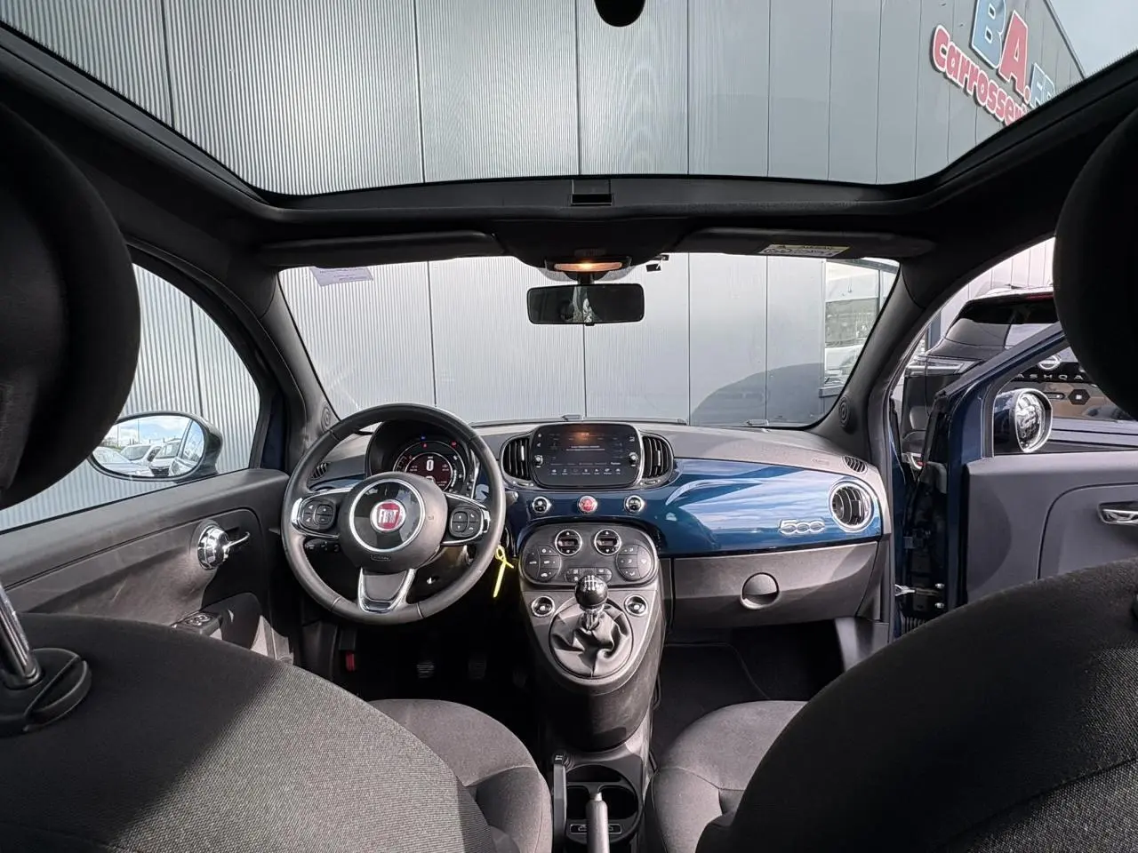Vue intérieure avant de la Fiat 500 Hybrid 70 bleu Dipinto avec tableau de bord brillant et toit panoramique.
