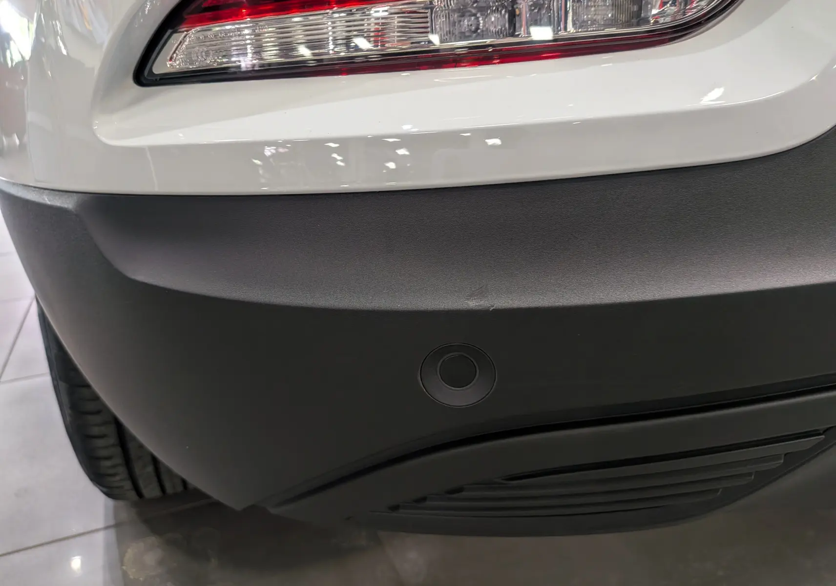 Gros plan sur le pare-chocs arrière noir et feu arrière droit du Renault Kadjar blanc Glacier, avec capteur de recul visible.