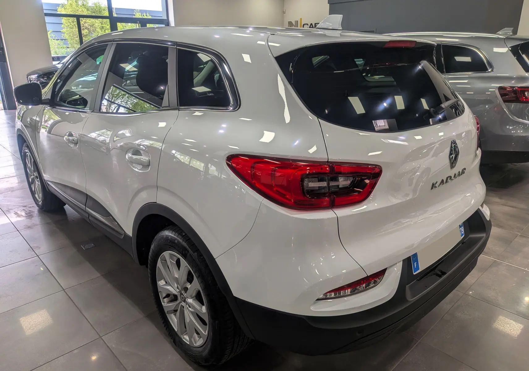 Renault Kadjar Blanc Glacier vu en 3/4 arrière droit, avec feux arrière rouges et jantes alliage en showroom.