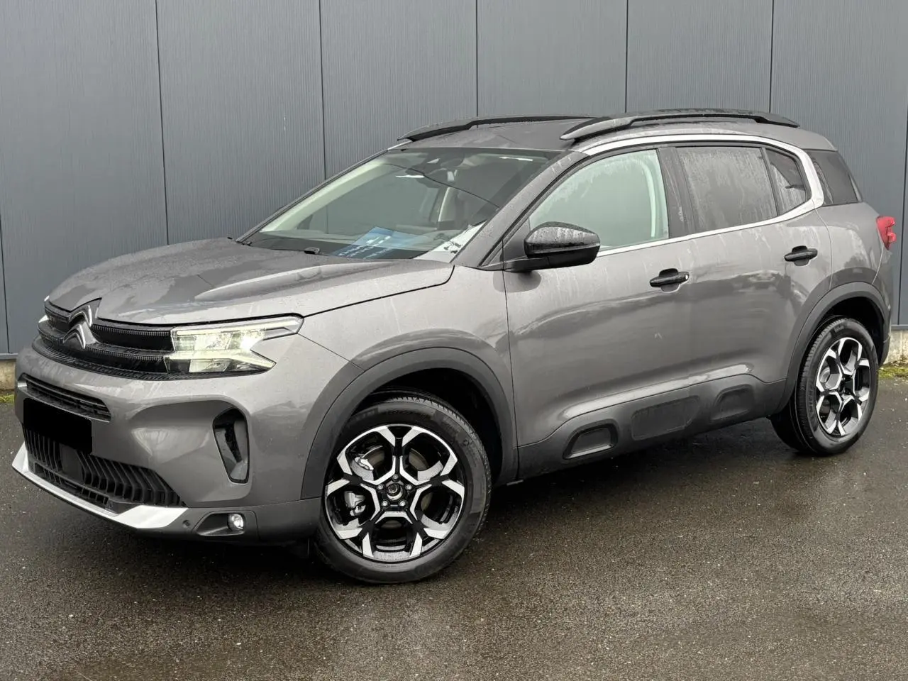 Vue 3/4 avant droite d’un Citroën C5 Aircross gris Platinium avec jantes alliage bi-ton et barres de toit noires.