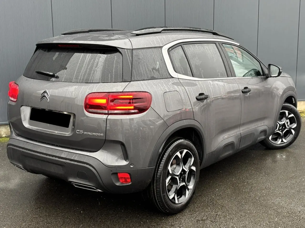 Vue 3/4 arrière droite du Citroën C5 Aircross gris Platinium avec feux arrière allumés et jantes alliage bi-ton.