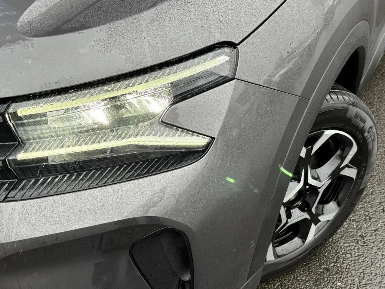 Gros plan sur l'avant droit gris Platinium du Citroën C5 Aircross 2025, mettant en valeur le phare LED et la jante alliage bi-ton.