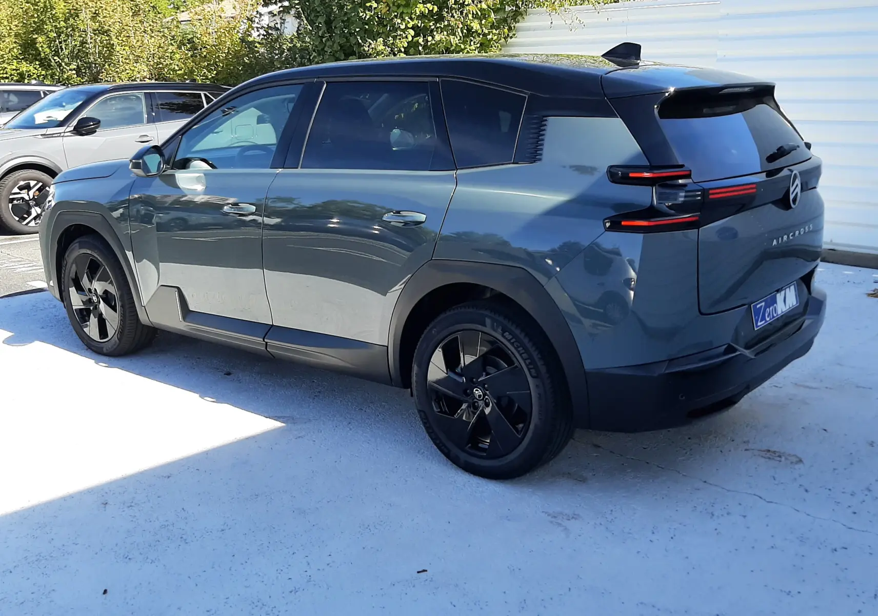 Vue 3/4 arrière droite du Citroën C5 Aircross vert Astoria avec toit noir et jantes noires sur parking extérieur.