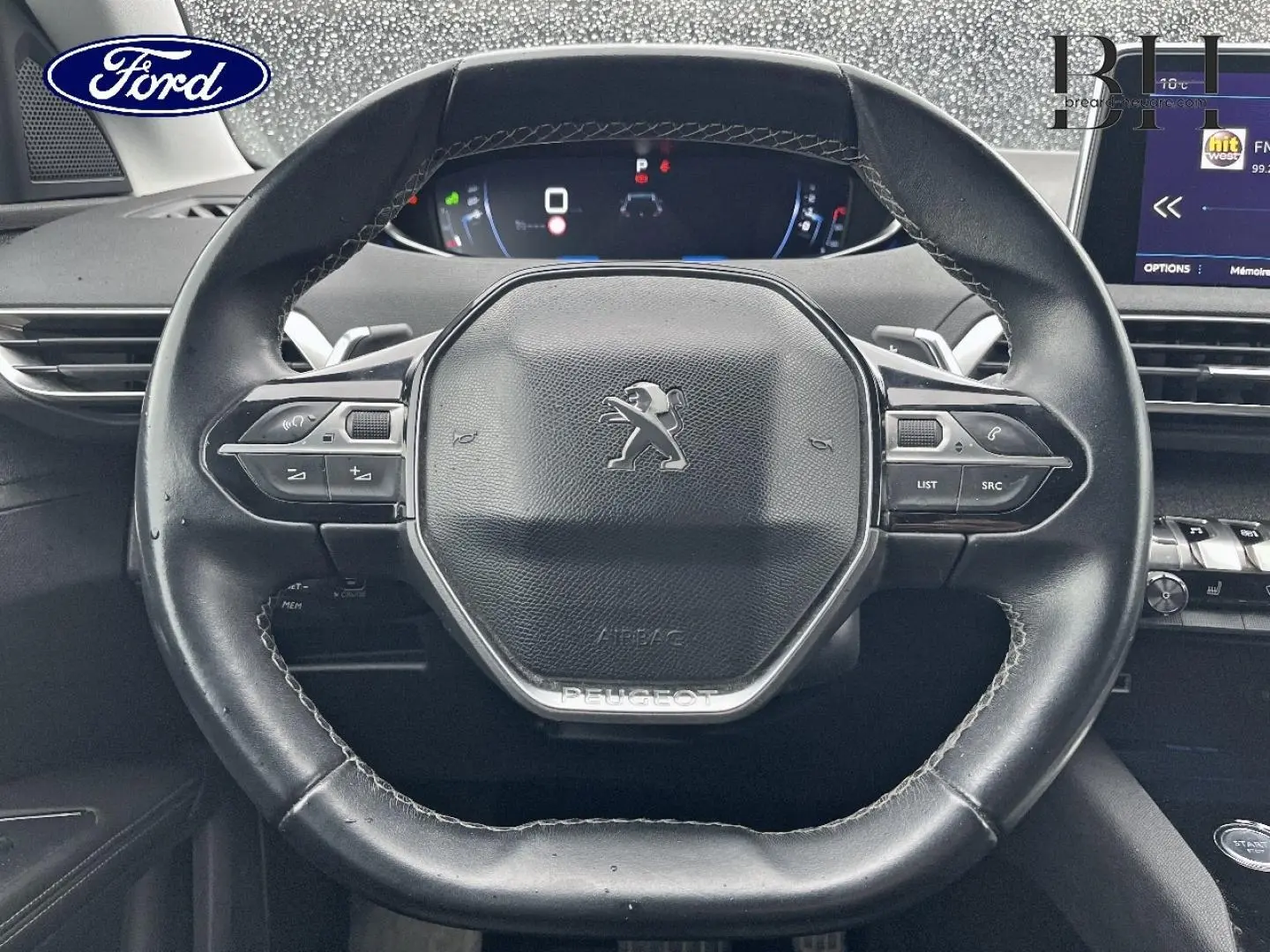 Vue rapprochée du volant cuir noir multifonction d'un Peugeot 5008 avec tableau de bord numérique et écran tactile à droite.