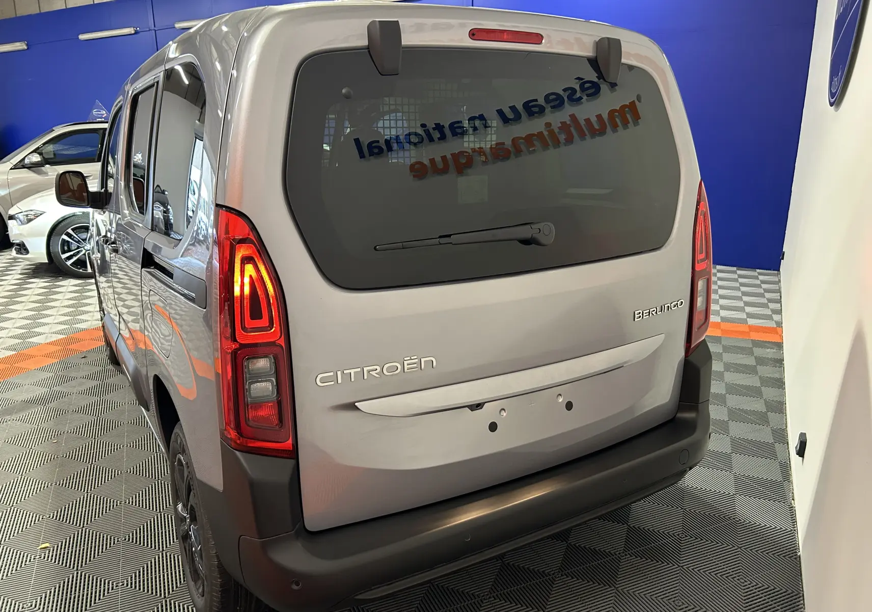 Vue 3/4 arrière d'un Citroën Berlingo Multispace gris Artense avec feux arrière allumés en intérieur showroom.