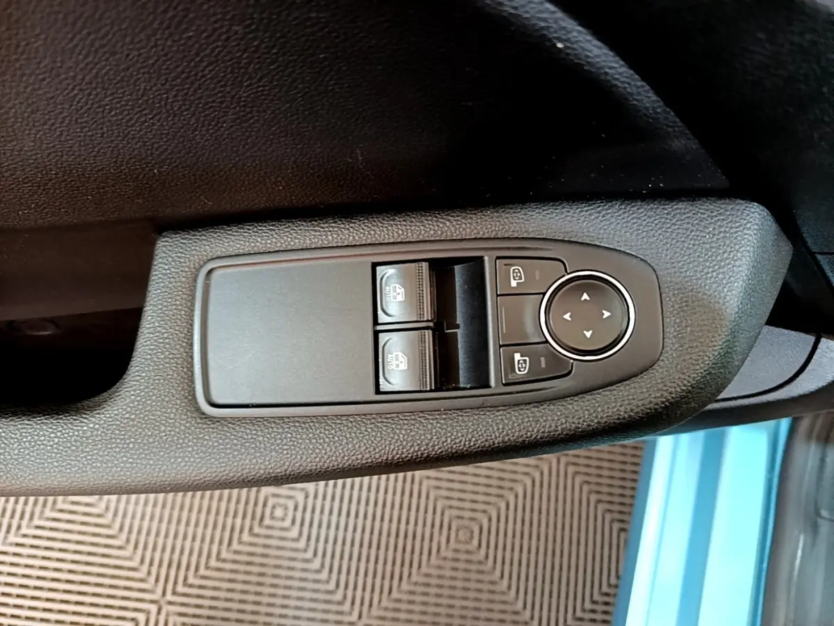 Vue rapprochée des commandes de réglage des vitres et des rétroviseurs sur la porte côté conducteur d'une Renault Clio bleu.