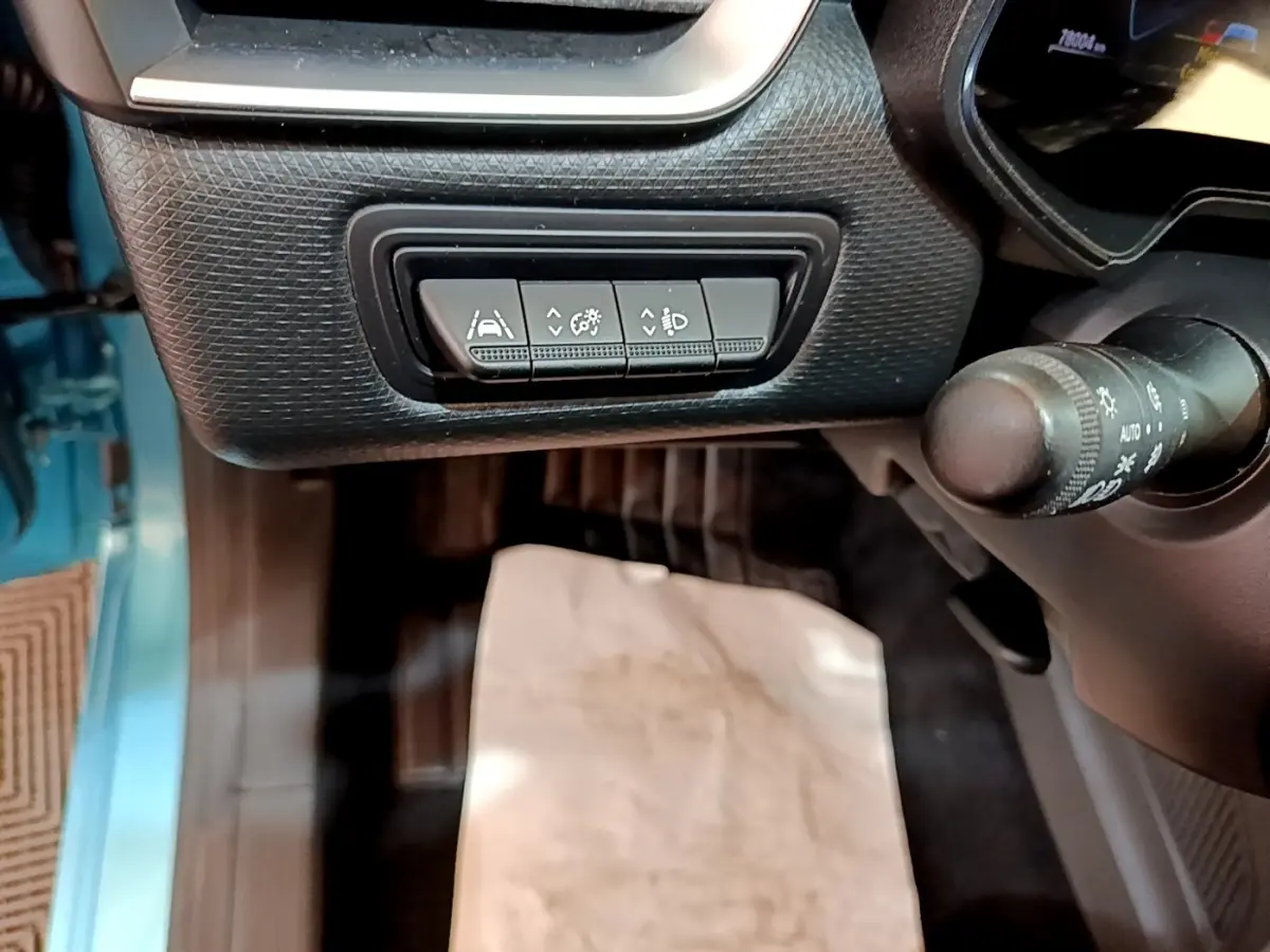Gros plan sur les commandes d’aide à la conduite sous le tableau de bord côté conducteur d’une Renault Clio bleu hybride 2021.