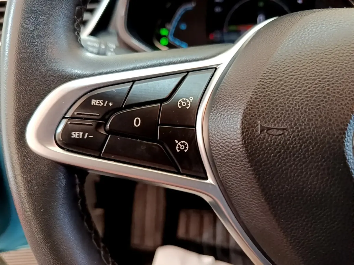 Gros plan sur les commandes du régulateur de vitesse au volant en cuir synthétique de la Renault Clio Business E-Tech hybride bleu.