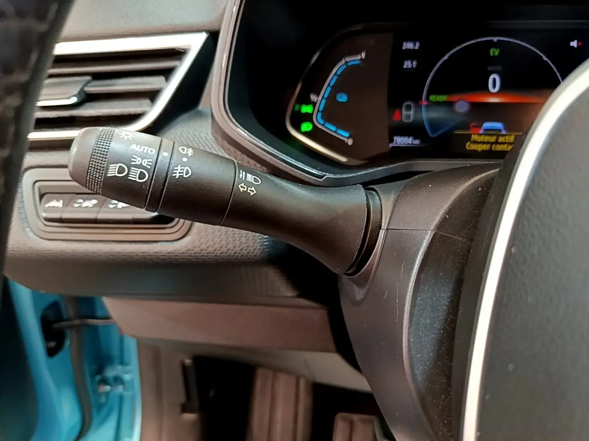 Gros plan sur la commande des phares et clignotants à gauche du volant dans l’habitacle bleu d’une Renault Clio hybride.