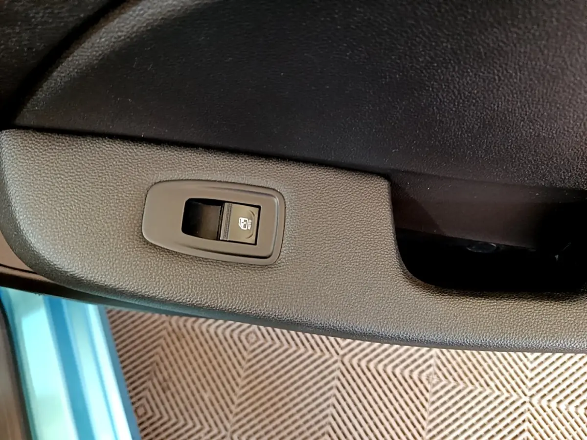 Gros plan sur le bouton de commande de la vitre électrique côté porte intérieure d’une Renault Clio Business E-Tech hybride bleu.