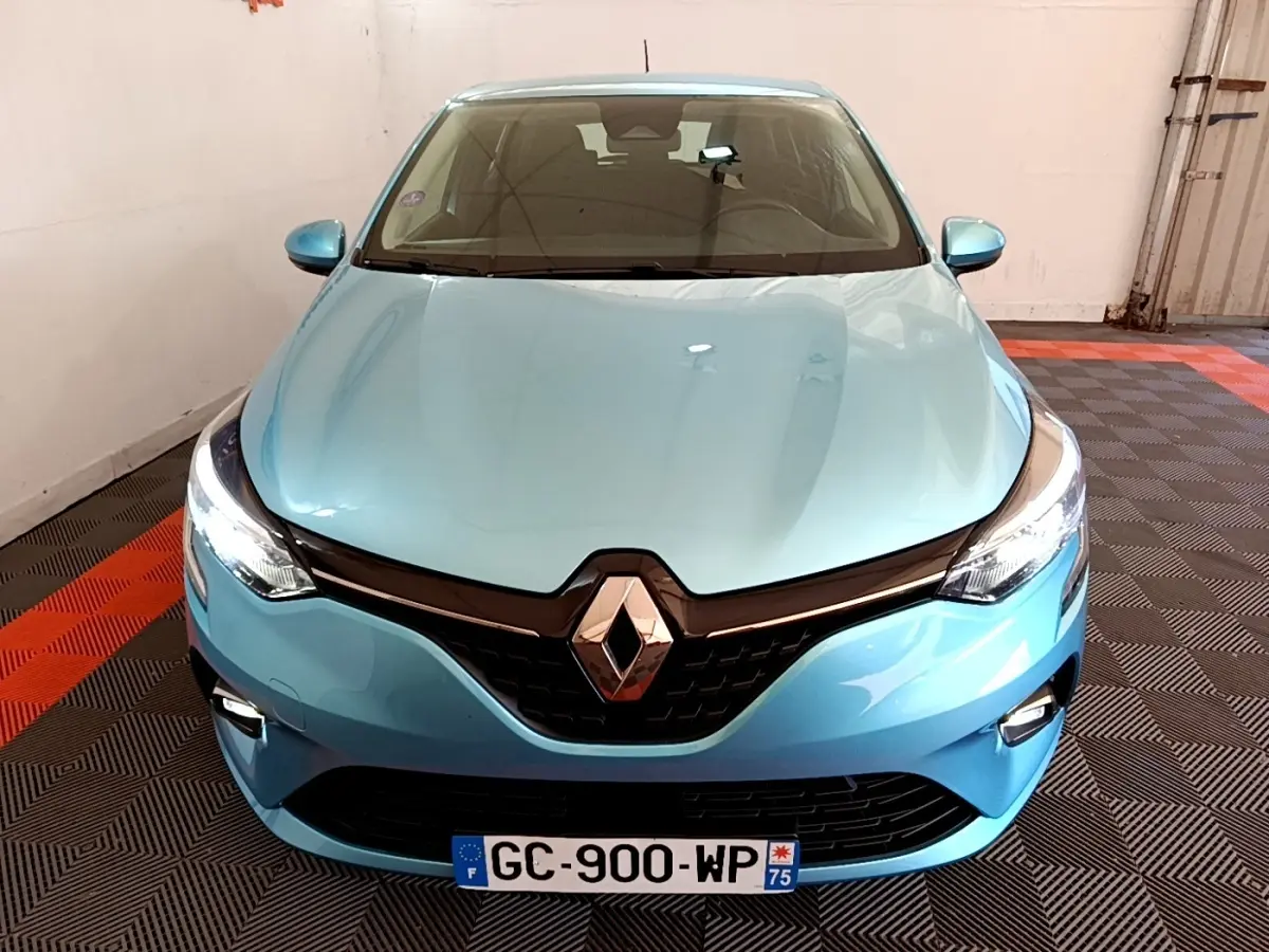 Vue avant rapprochée d'une Renault Clio Business E-Tech hybride bleu clair avec phares LED allumés en intérieur.
