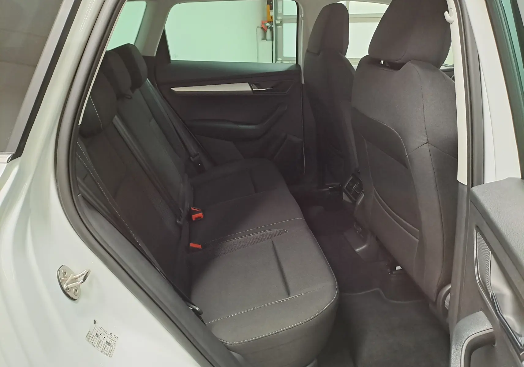Vue intérieure arrière côté gauche du Skoda Karoq blanc Lune, montrant les sièges arrière en tissu noir et les finitions sobres.