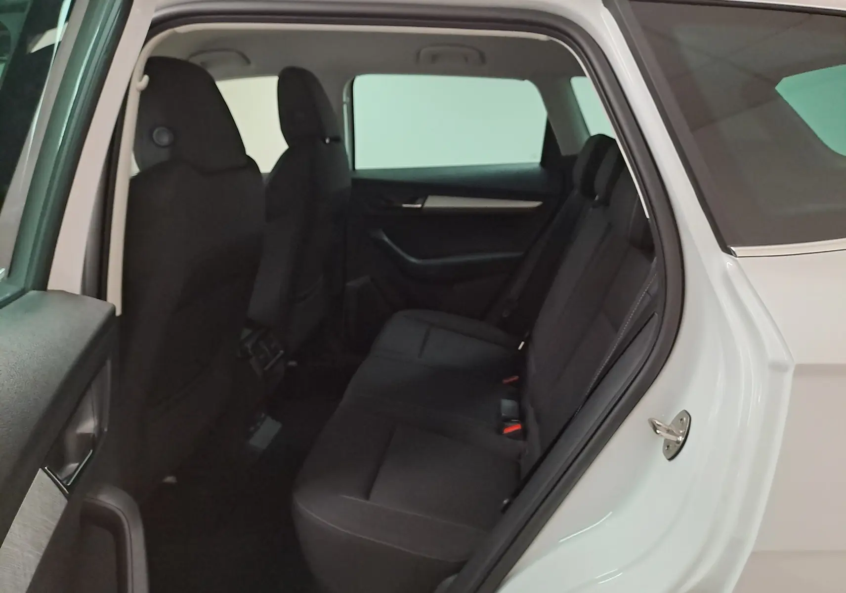 Vue côté gauche arrière sur l’intérieur du Skoda Karoq blanc Lune, montrant les sièges arrière noirs et la porte ouverte.