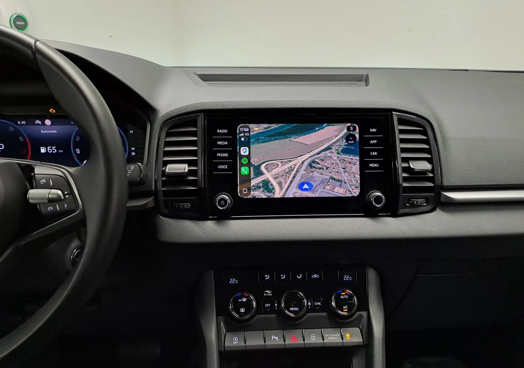 Vue intérieure centrée sur le tableau de bord et l'écran tactile du Skoda Karoq 1.5 TSI blanc Lune, avec commandes climatisation visibles.