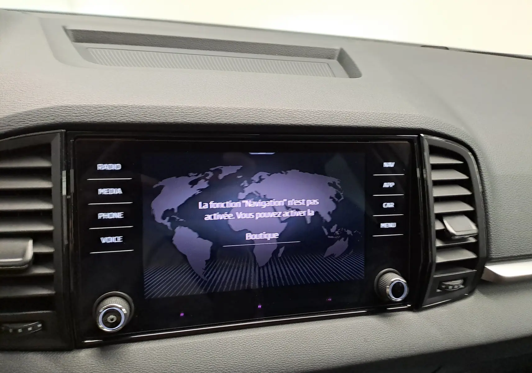 Écran tactile central du Skoda Karoq 2025 affichant un message de navigation, entouré de commandes et grilles d’aération.
