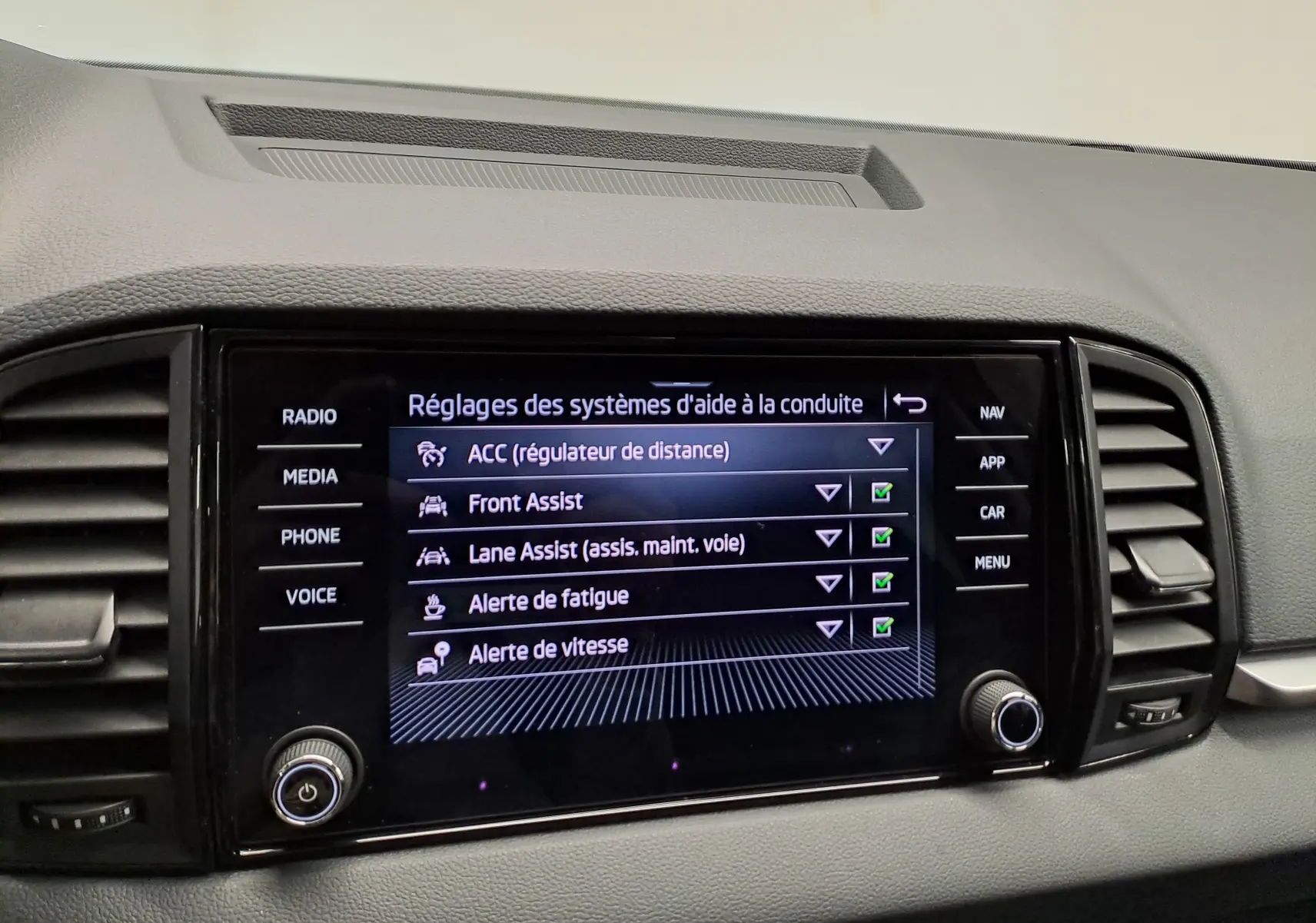 Écran central du tableau de bord du Skoda Karoq blanc Lune, affichant les réglages des aides à la conduite.