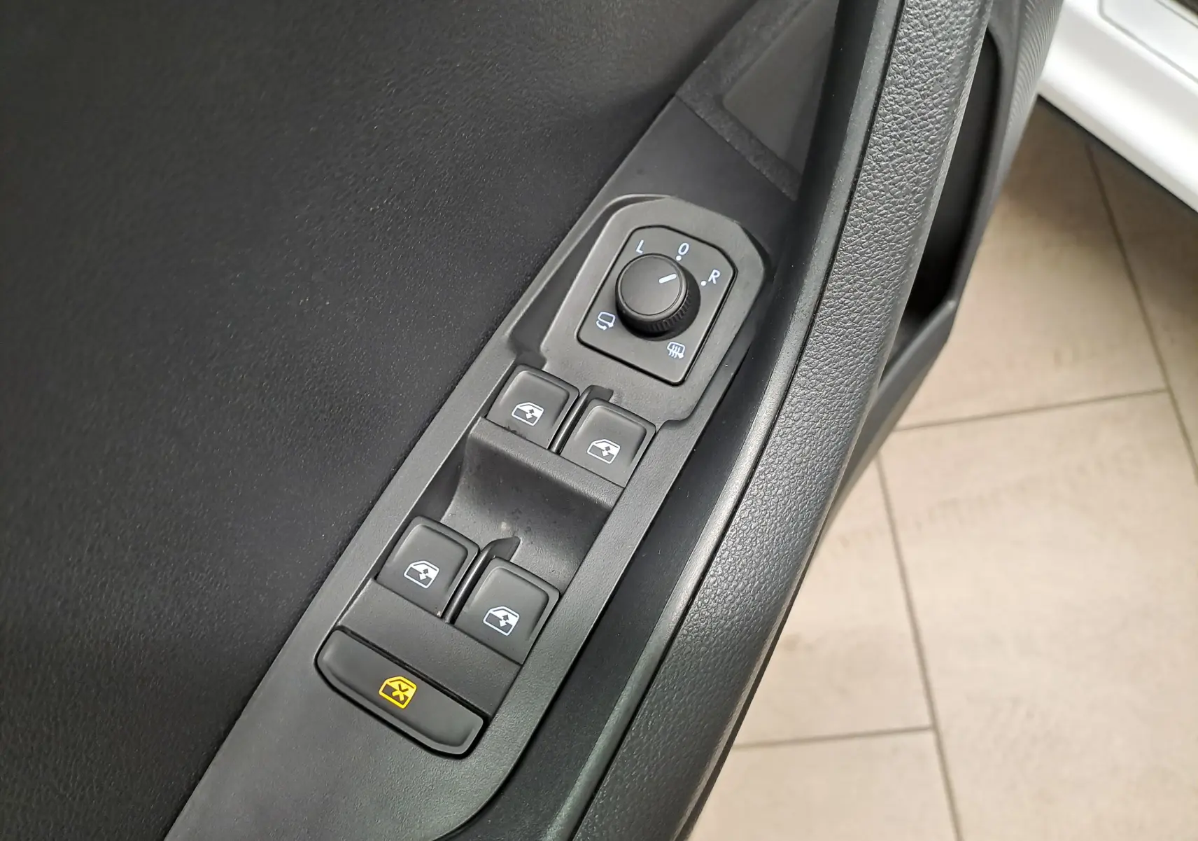 Gros plan sur les commandes de lève-vitres et réglage des rétroviseurs côté conducteur d’un Skoda Karoq blanc Lune.