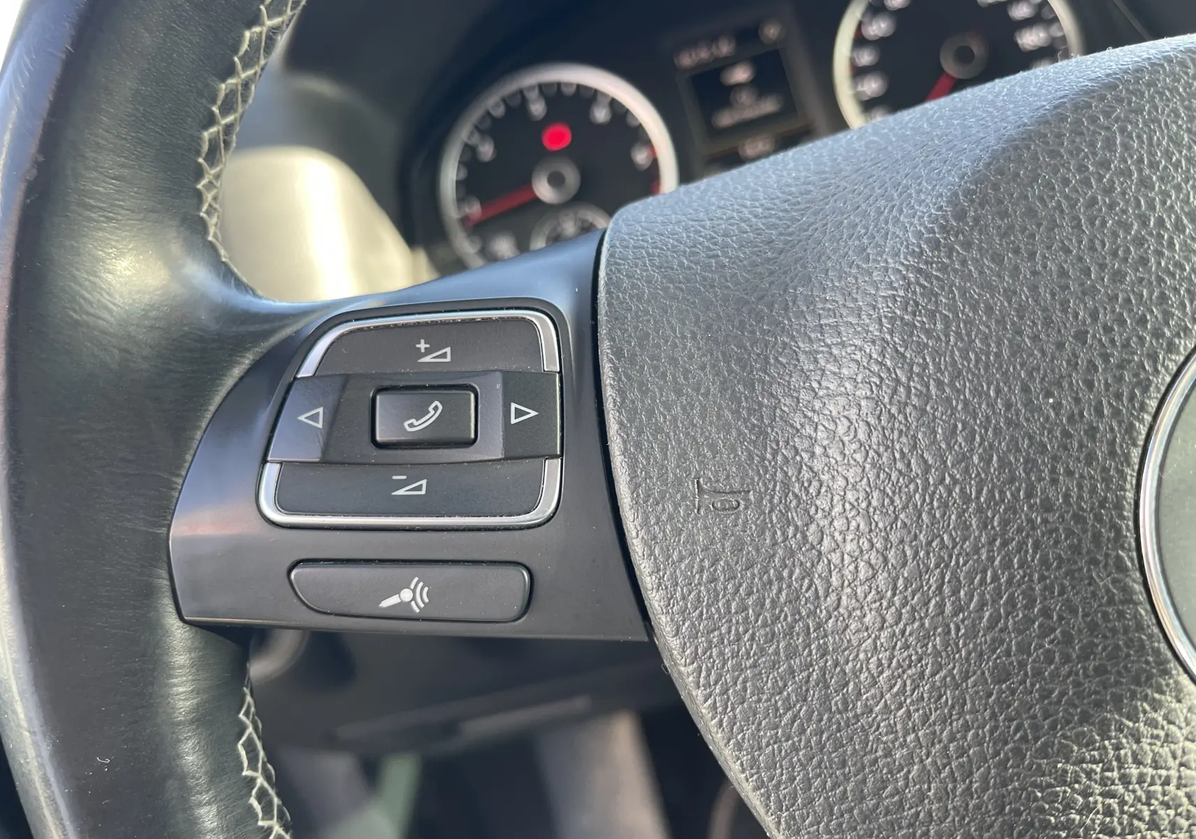 Gros plan sur les commandes au volant à gauche du Volkswagen Tiguan gris foncé, tableau de bord en arrière-plan flou.