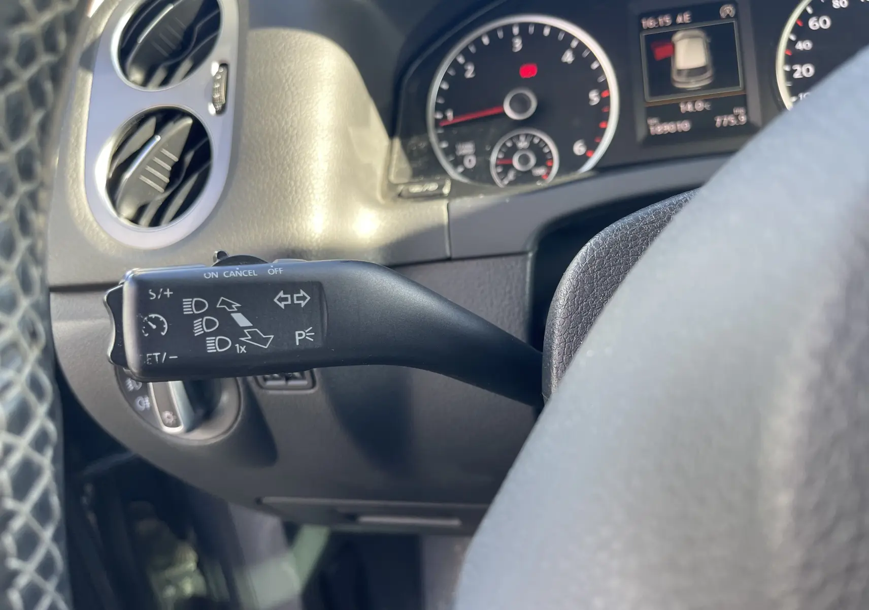 Gros plan sur le commodo gauche du tableau de bord gris foncé du Volkswagen Tiguan 2015, avec compteurs en arrière-plan.