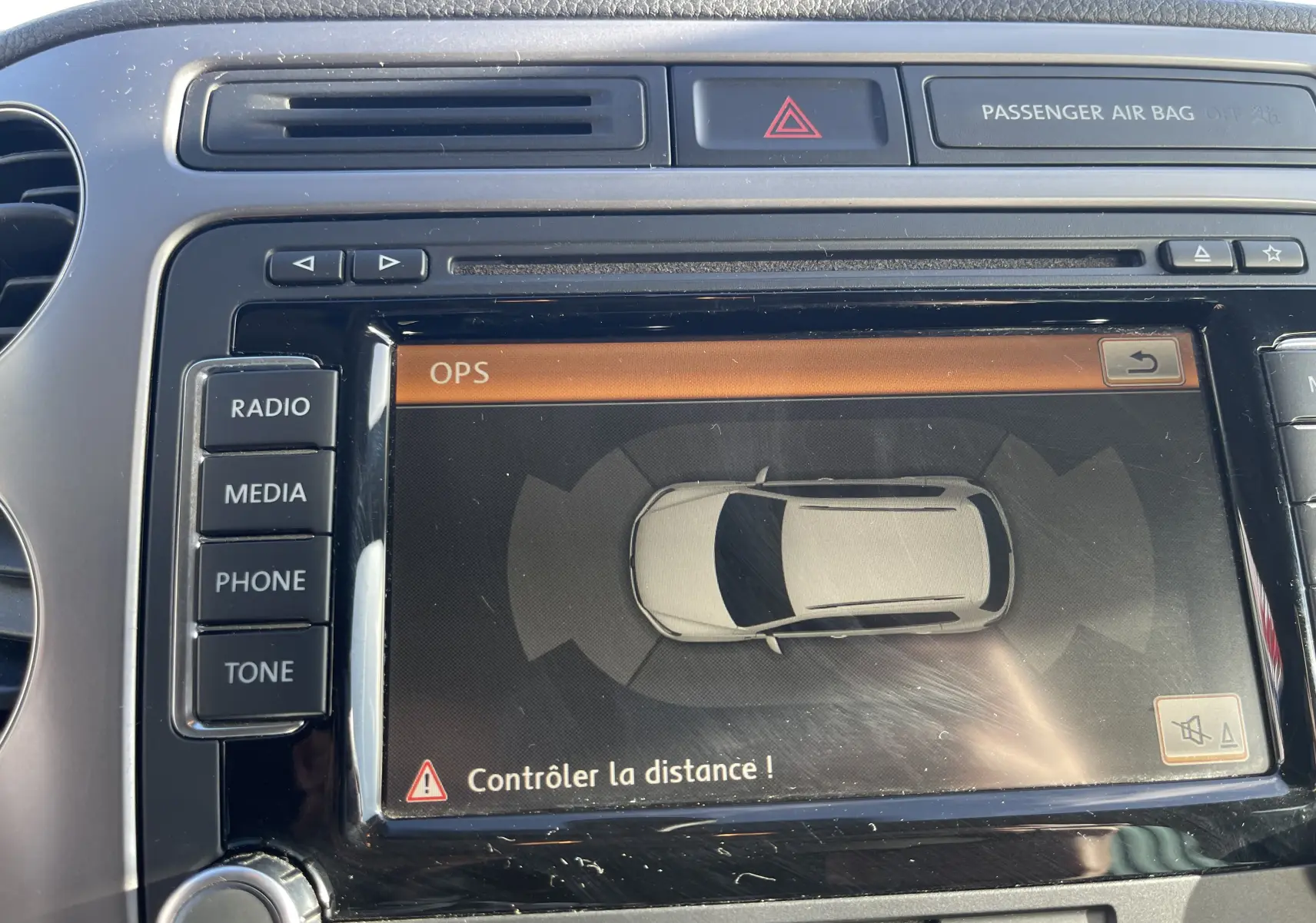 Écran central du Volkswagen Tiguan 2015 gris foncé montrant l'alerte de contrôle de distance en vue intérieure frontale.