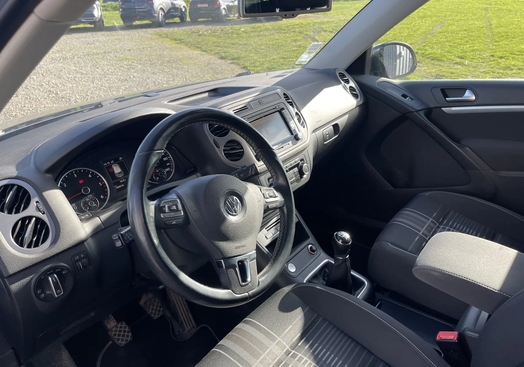 Vue intérieure côté conducteur du Volkswagen Tiguan gris foncé 2015, avec volant multifonction et boîte manuelle.