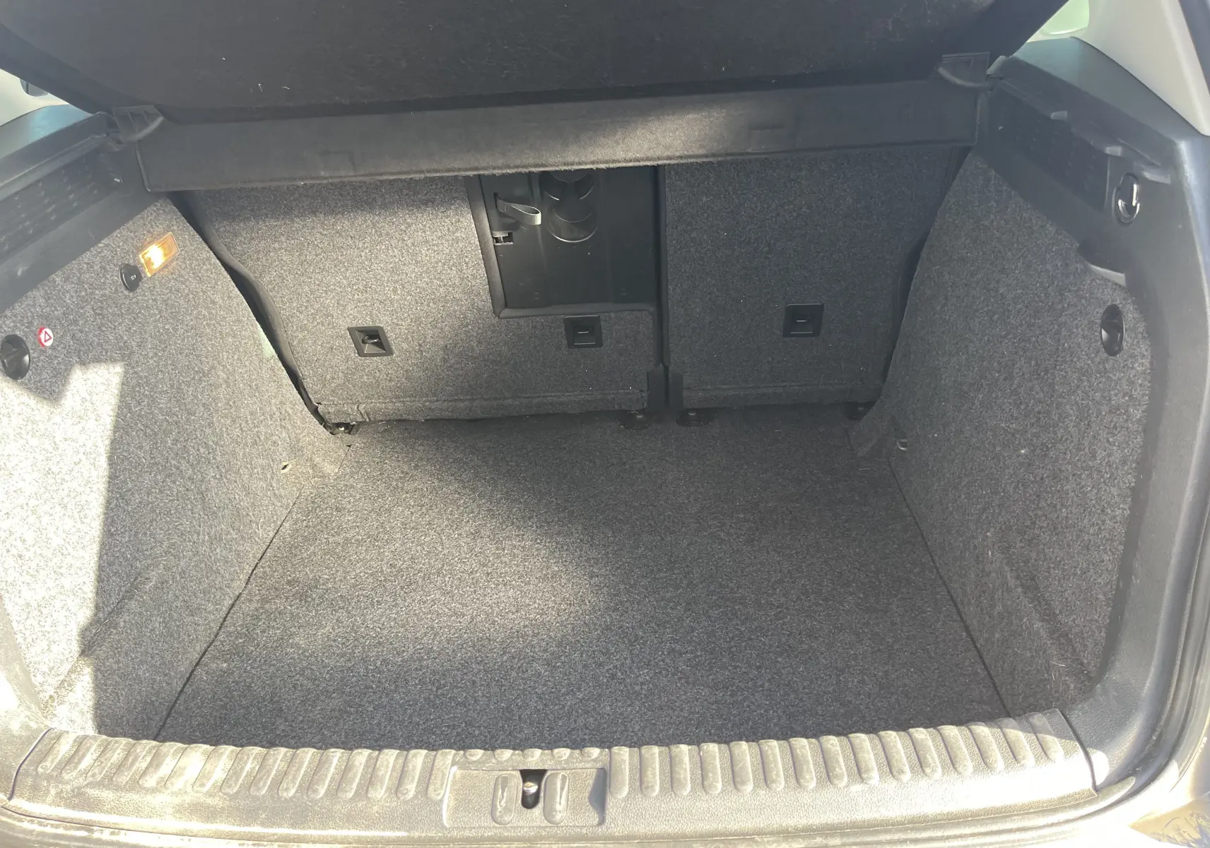 Coffre ouvert du Volkswagen Tiguan gris foncé 2015, vue intérieure montrant l'espace de chargement vide et revêtement en tissu gris.