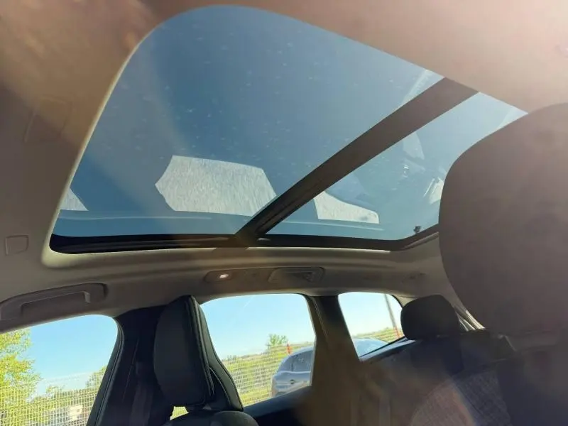 Vue intérieure du toit panoramique en verre du Volvo XC60 gris, avec sièges avant visibles et lumière naturelle.