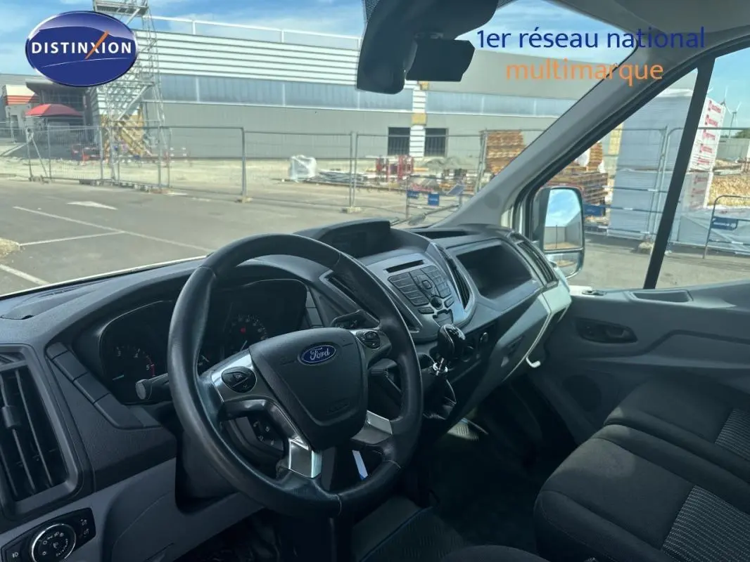 Vue intérieure du poste de conduite du Ford Transit Fourgon blanc, montrant le volant multifonction et la console centrale.