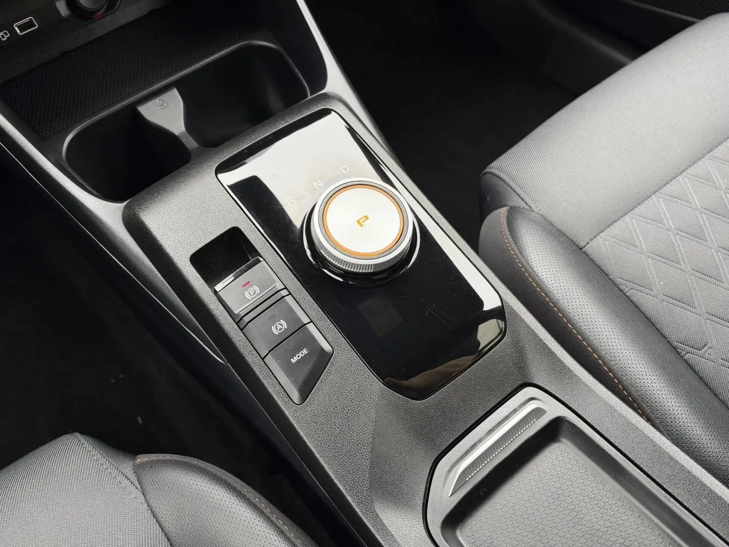 Gros plan sur la console centrale noire et la molette de boîte automatique du MG3 1.5 Hybrid+ 195ch Luxury, sièges gris.