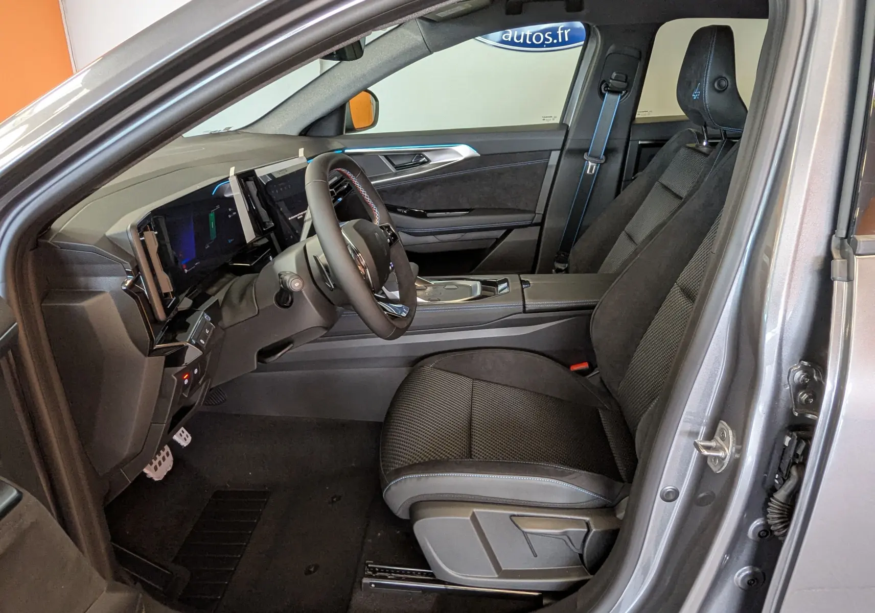 Intérieur côté conducteur du Renault Austral gris schist 2025, sièges noirs avec surpiqûres bleues et tableau de bord digital.